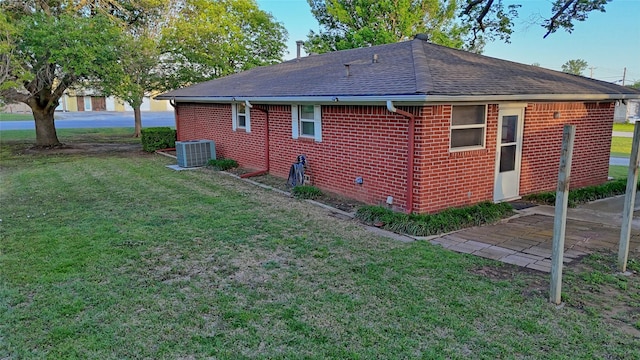 back of property featuring a yard, central AC unit, a shingled roof, and brick siding
