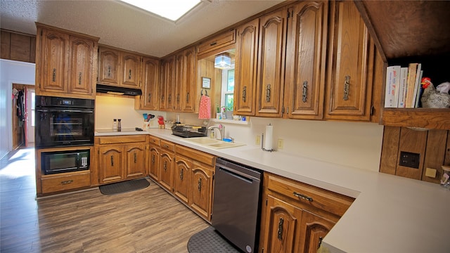 kitchen featuring brown cabinetry, black appliances, light wood-style floors, and a sink