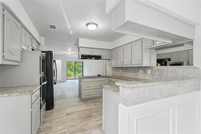 829 Hunters Creek Dr, Desoto, TX 75115 - kitchen with under cabinet range hood, oven, visible vents, light wood-style flooring, and a peninsula