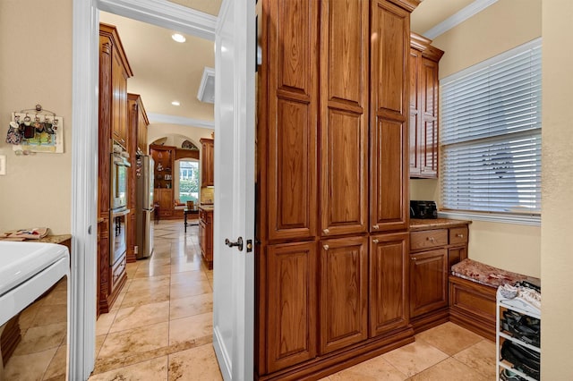 interior space with ornamental molding, arched walkways, and brown cabinetry