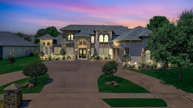 french provincial home with stucco siding, curved driveway, french doors, and stone siding