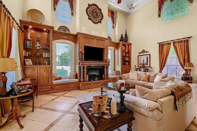 living area with a towering ceiling, a glass covered fireplace, a wealth of natural light, and crown molding