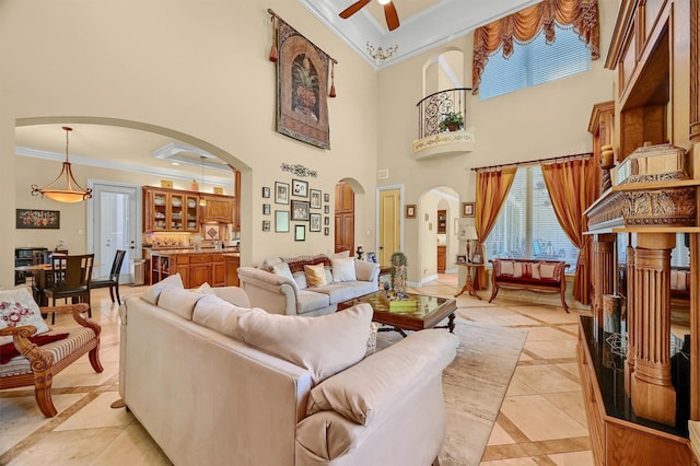 living room with light tile patterned floors, ceiling fan, arched walkways, ornamental molding, and a towering ceiling