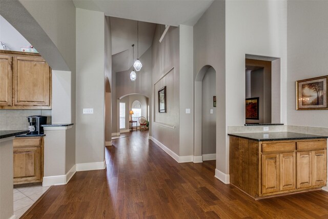 kitchen with dark wood-type flooring, baseboards, high vaulted ceiling, and arched walkways