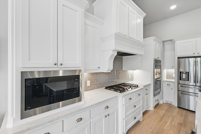 kitchen featuring light wood-type flooring, white cabinetry, stainless steel appliances, and decorative backsplash