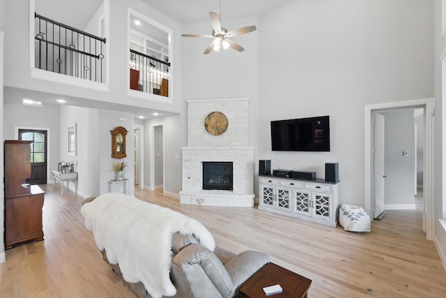 living area with a high ceiling, a ceiling fan, wood finished floors, and a fireplace