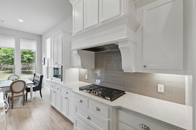 kitchen featuring light stone counters, decorative backsplash, white cabinets, appliances with stainless steel finishes, and light wood finished floors