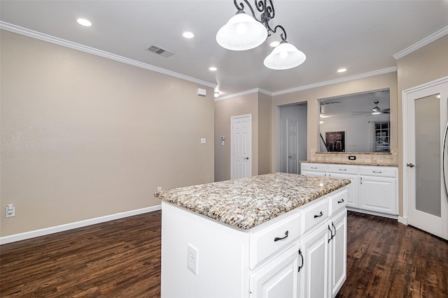 kitchen with dark wood finished floors, visible vents, ornamental molding, and a kitchen island