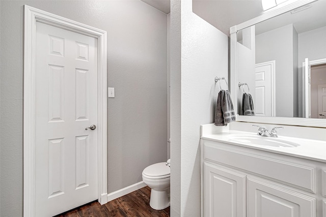 bathroom with toilet, vanity, wood finished floors, and baseboards