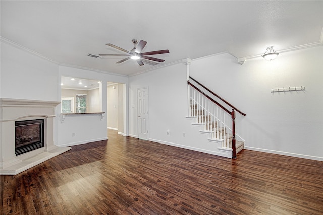 unfurnished living room with wood finished floors, stairs, ornamental molding, ceiling fan, and a glass covered fireplace