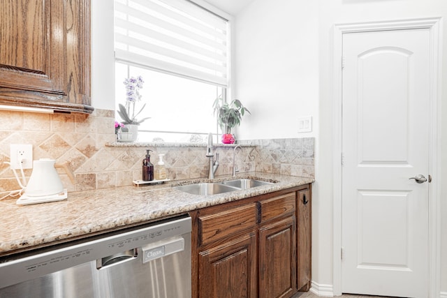 kitchen featuring light stone counters, decorative backsplash, stainless steel dishwasher, and a sink