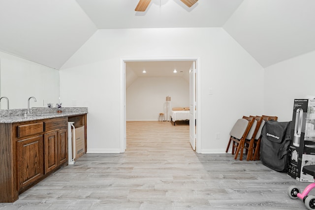 bar featuring a ceiling fan, light wood finished floors, vaulted ceiling, and a sink