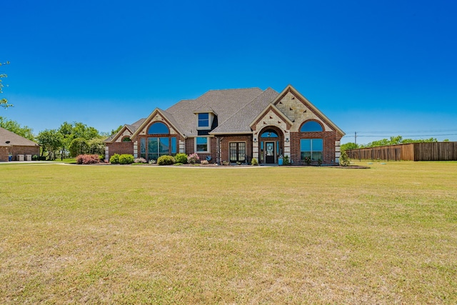 french provincial home with fence, a front lawn, and brick siding