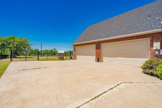 view of side of property featuring fence, concrete driveway, a shingled roof, and brick siding
