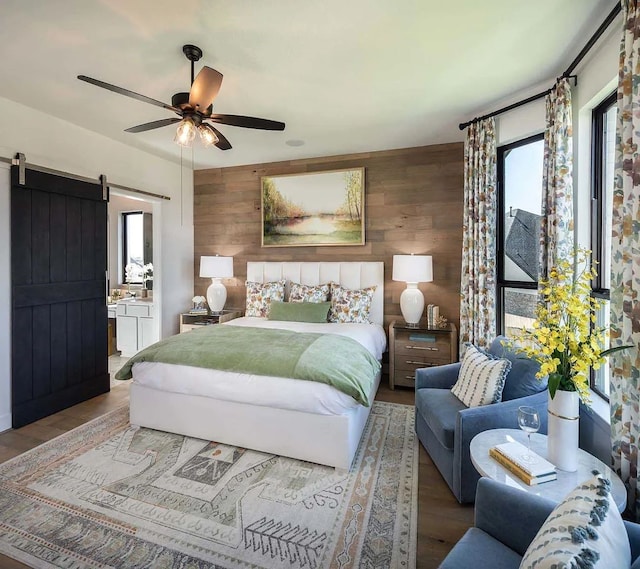bedroom featuring a barn door, wood finished floors, wooden walls, and connected bathroom