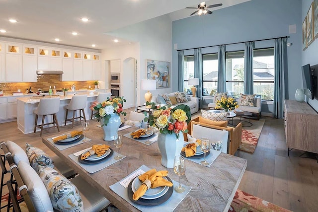 dining room with recessed lighting, arched walkways, light wood finished floors, a ceiling fan, and a high ceiling