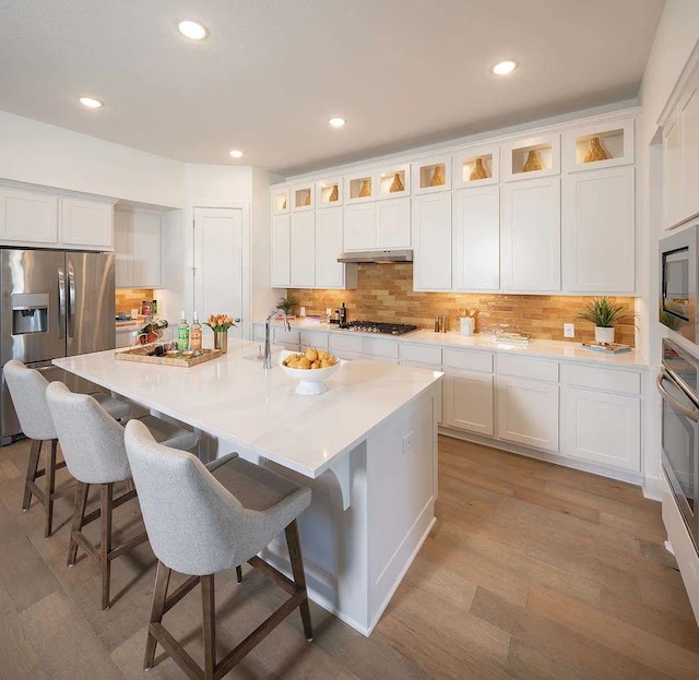 kitchen with appliances with stainless steel finishes, tasteful backsplash, an island with sink, and under cabinet range hood