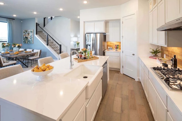 kitchen featuring recessed lighting, decorative backsplash, stainless steel appliances, a center island with sink, and white cabinetry