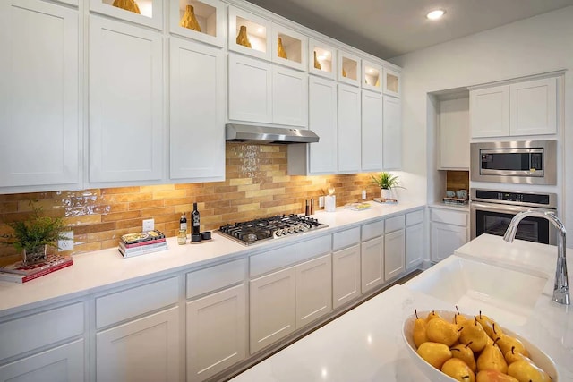 kitchen featuring decorative backsplash, white cabinets, appliances with stainless steel finishes, light countertops, and under cabinet range hood