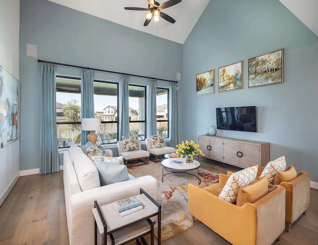 living area with a ceiling fan, high vaulted ceiling, wood finished floors, and baseboards