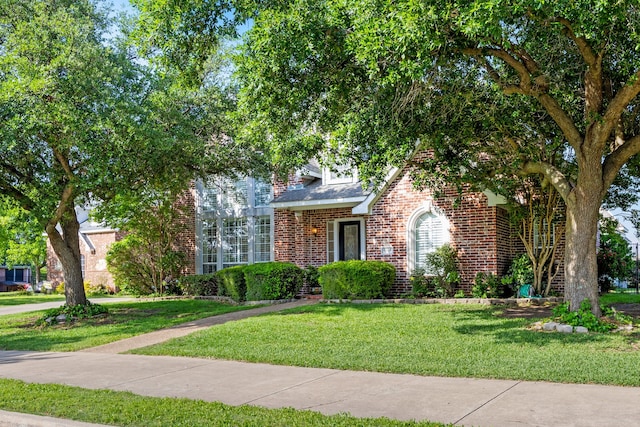 view of property hidden behind natural elements featuring roof with shingles, a front lawn, and brick siding