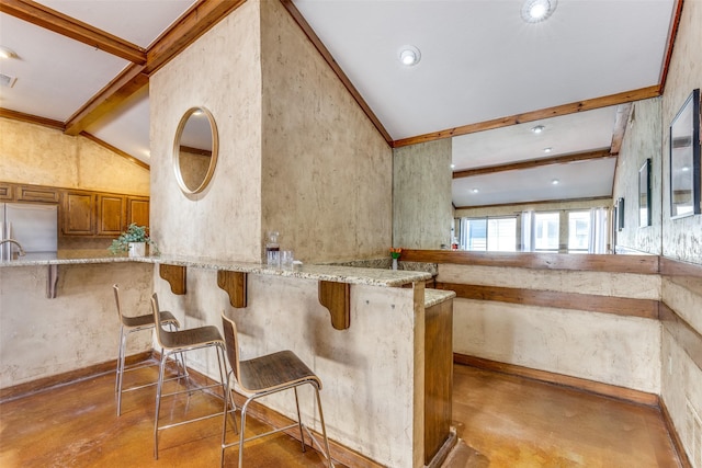 kitchen featuring built in refrigerator, light stone counters, a kitchen breakfast bar, and brown cabinets