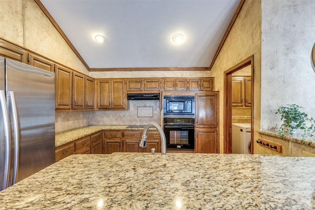 kitchen featuring decorative backsplash, brown cabinetry, vaulted ceiling, black appliances, and washer / clothes dryer