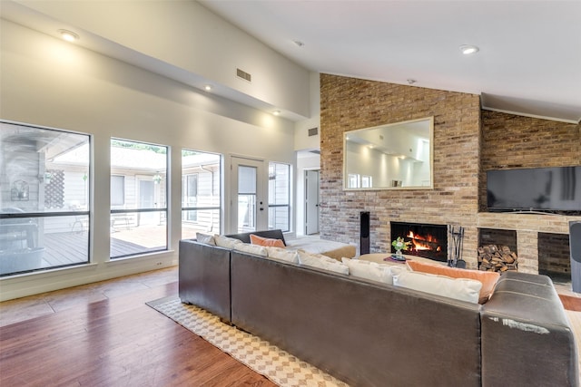 living area with brick wall, a brick fireplace, high vaulted ceiling, visible vents, and wood finished floors