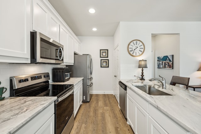 kitchen featuring light stone counters, white cabinetry, tasteful backsplash, a sink, and stainless steel appliances