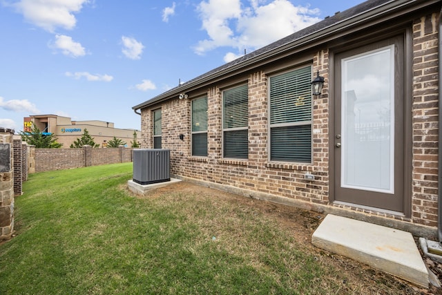 exterior space with a lawn, central air condition unit, fence, and brick siding