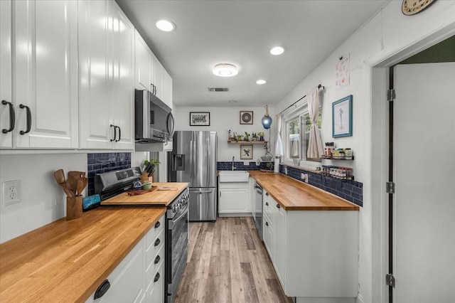 kitchen featuring white cabinets, visible vents, stainless steel appliances, and butcher block countertops