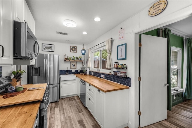 kitchen featuring a sink, stainless steel appliances, visible vents, white cabinetry, and butcher block counters