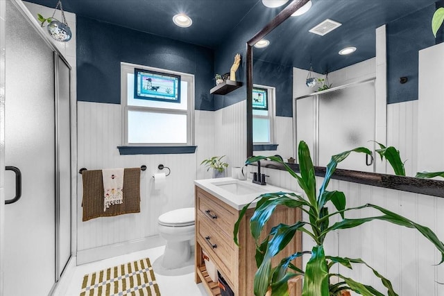 bathroom featuring vanity, toilet, a stall shower, a wainscoted wall, and visible vents