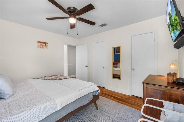 bedroom with a ceiling fan, visible vents, wood finished floors, and baseboards