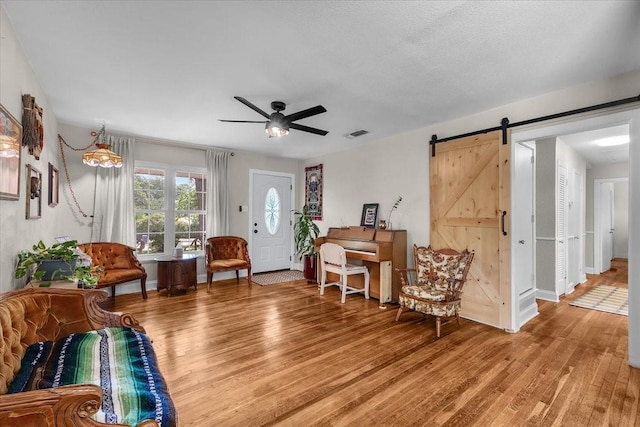 living area with visible vents, ceiling fan, a barn door, and light wood-type flooring