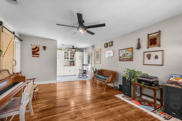 sitting room with a barn door, ceiling fan, visible vents, baseboards, and wood finished floors