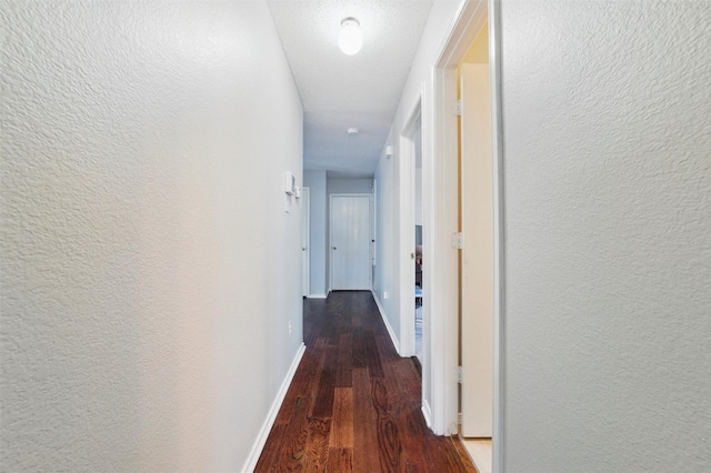 corridor featuring a textured wall, wood finished floors, and baseboards