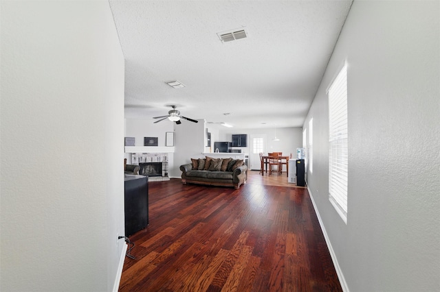 living room featuring dark wood-style flooring, visible vents, ceiling fan, and baseboards