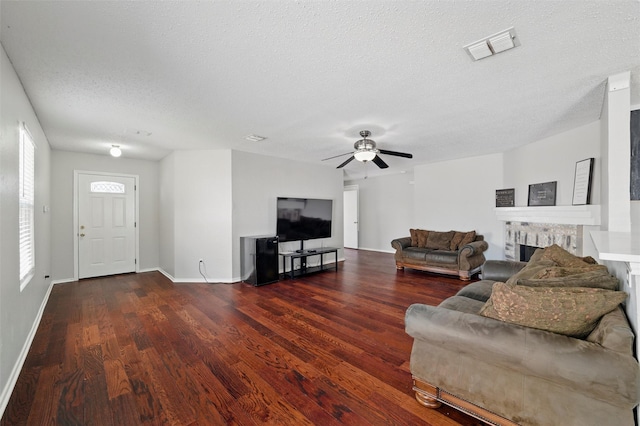 living area featuring wood finished floors, ceiling fan, a fireplace, visible vents, and a textured ceiling
