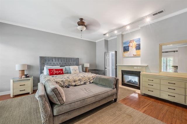 bedroom with wood finished floors, crown molding, visible vents, and a multi sided fireplace