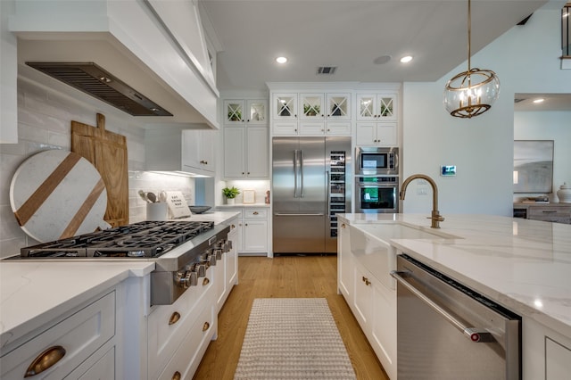 kitchen featuring light wood-style flooring, decorative backsplash, custom range hood, built in appliances, and a sink