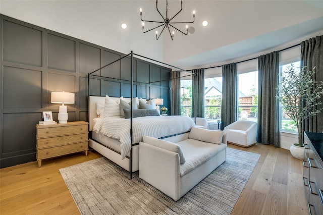 bedroom with light wood-style floors, recessed lighting, a decorative wall, a notable chandelier, and a high ceiling