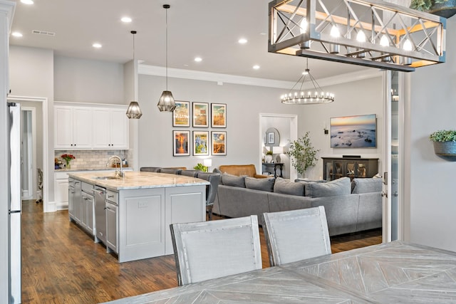 kitchen featuring tasteful backsplash, white cabinets, ornamental molding, a sink, and a center island with sink