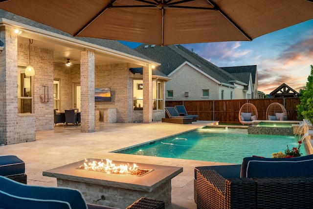 pool at dusk featuring an outdoor fire pit, fence, ceiling fan, a patio, and a pool with connected hot tub