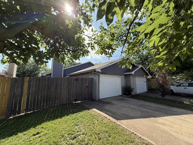 view of property exterior featuring fence, driveway, a lawn, and an attached garage
