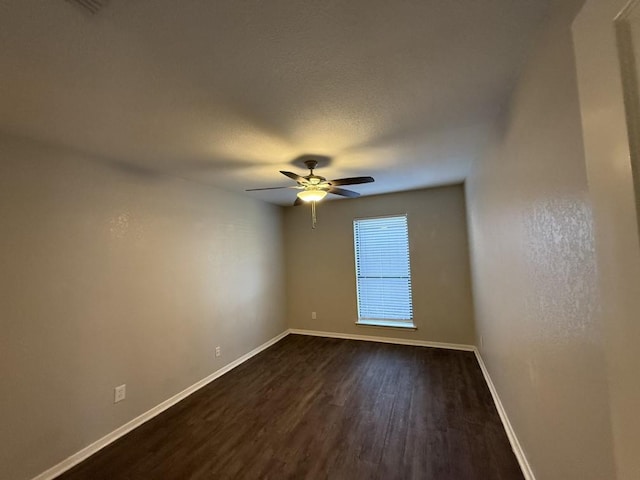 empty room with dark wood-type flooring, a ceiling fan, and baseboards