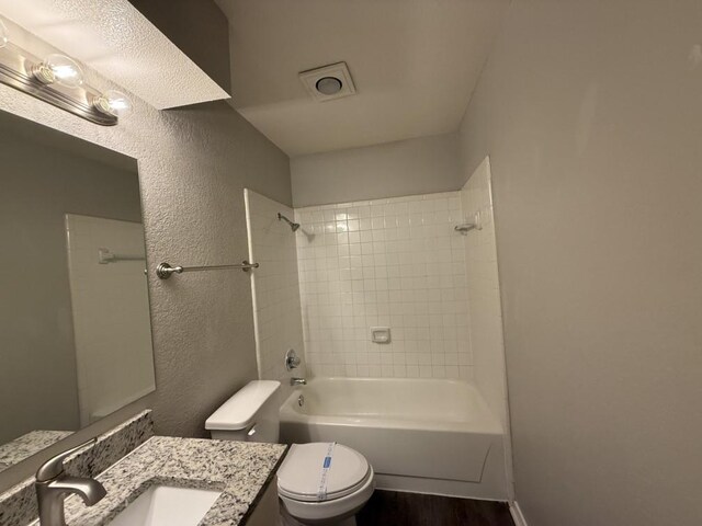 bathroom with vanity, bathing tub / shower combination, toilet, a textured wall, and wood finished floors
