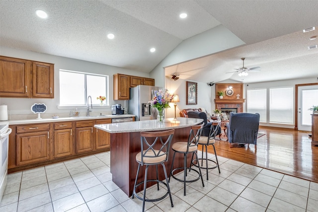 kitchen featuring brown cabinetry, stainless steel appliances, ceiling fan, a sink, and open floor plan