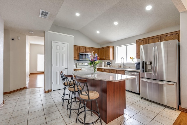 kitchen with a breakfast bar, stainless steel appliances, a kitchen island, a sink, and visible vents