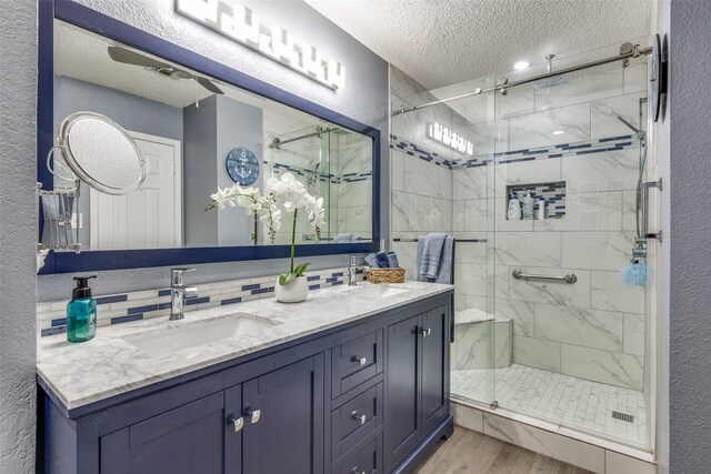 bathroom with wood finished floors, a textured wall, a sink, a stall shower, and a textured ceiling
